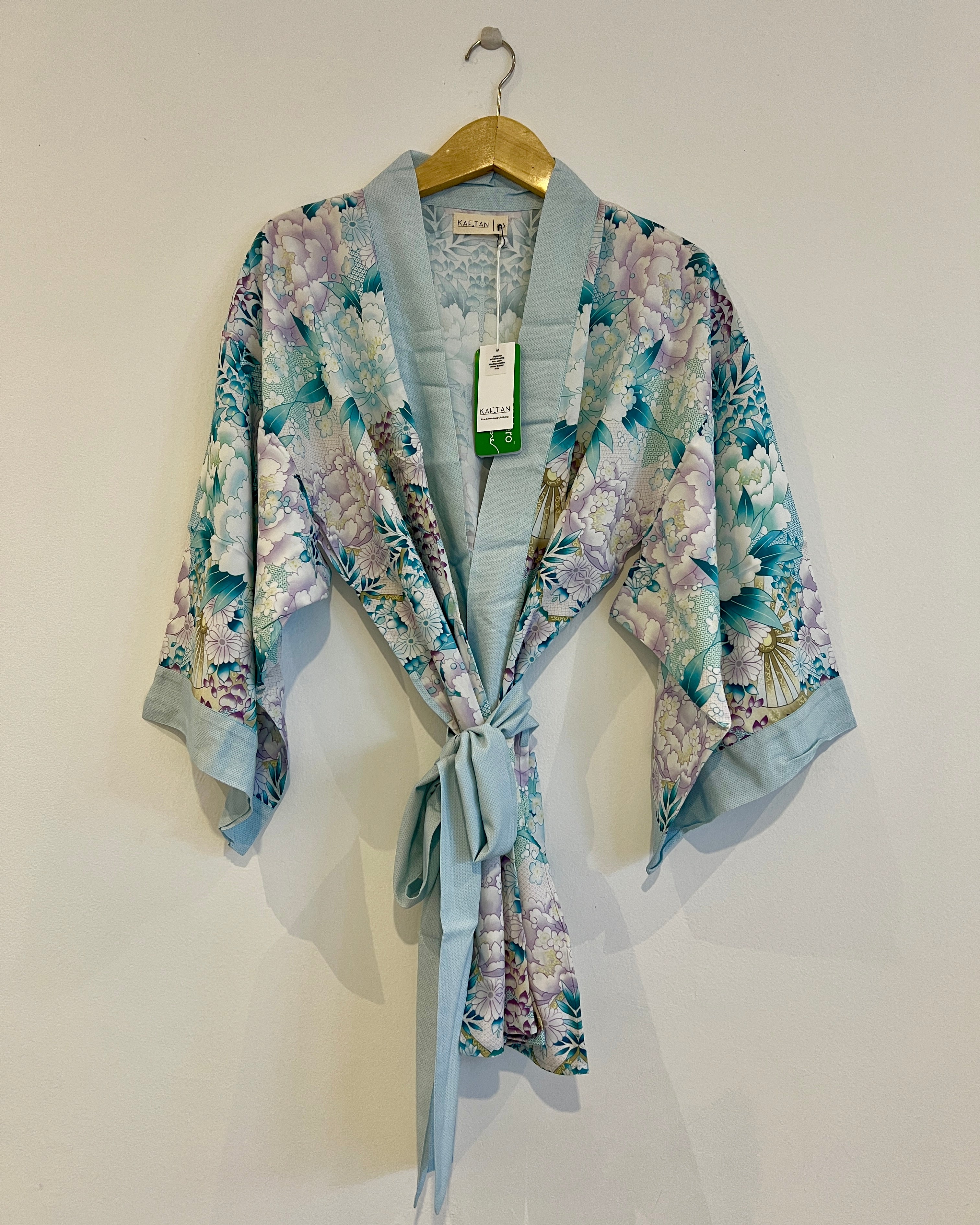 A floral kimono with wide sleeves, featuring a belt loop and a detachable waist tie, displayed on a hanger.