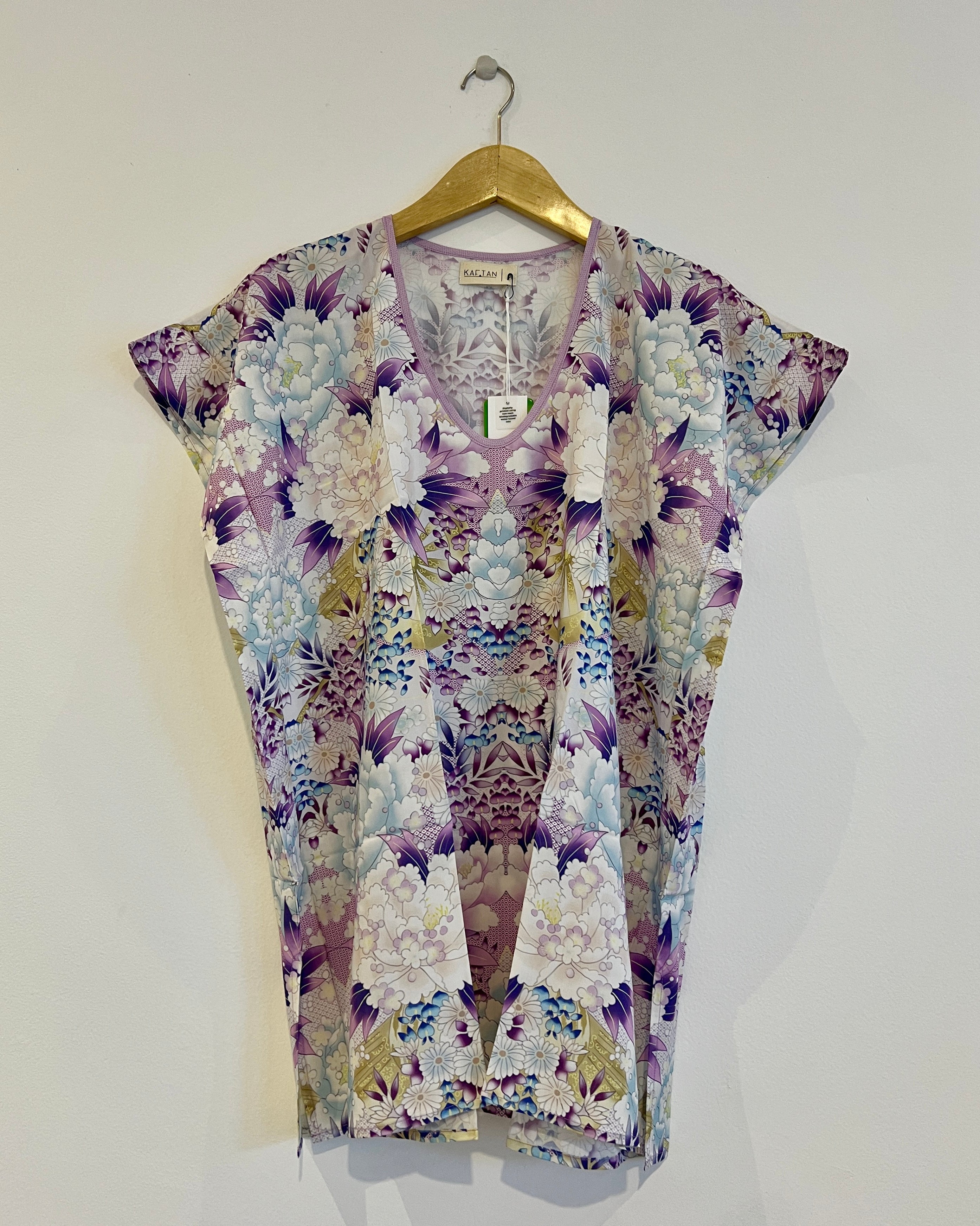 A short kaftan with a floral pattern, featuring a V-neck and thigh length. The garment is hanging on a wooden hanger against a white background.