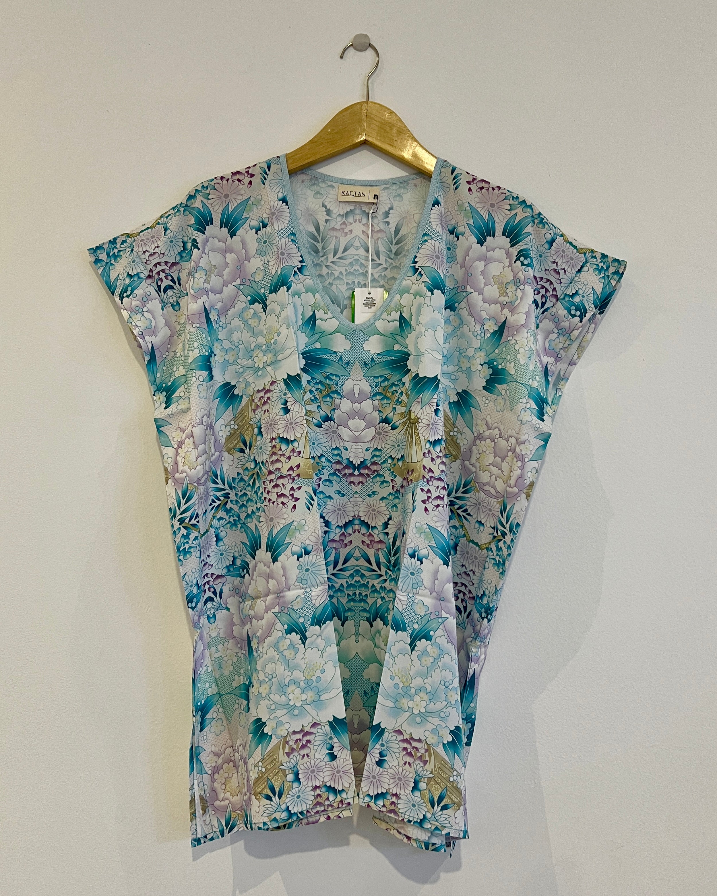 A short kaftan with a floral pattern, featuring a V-neck and thigh length. The garment is hanging on a wooden hanger against a white background.