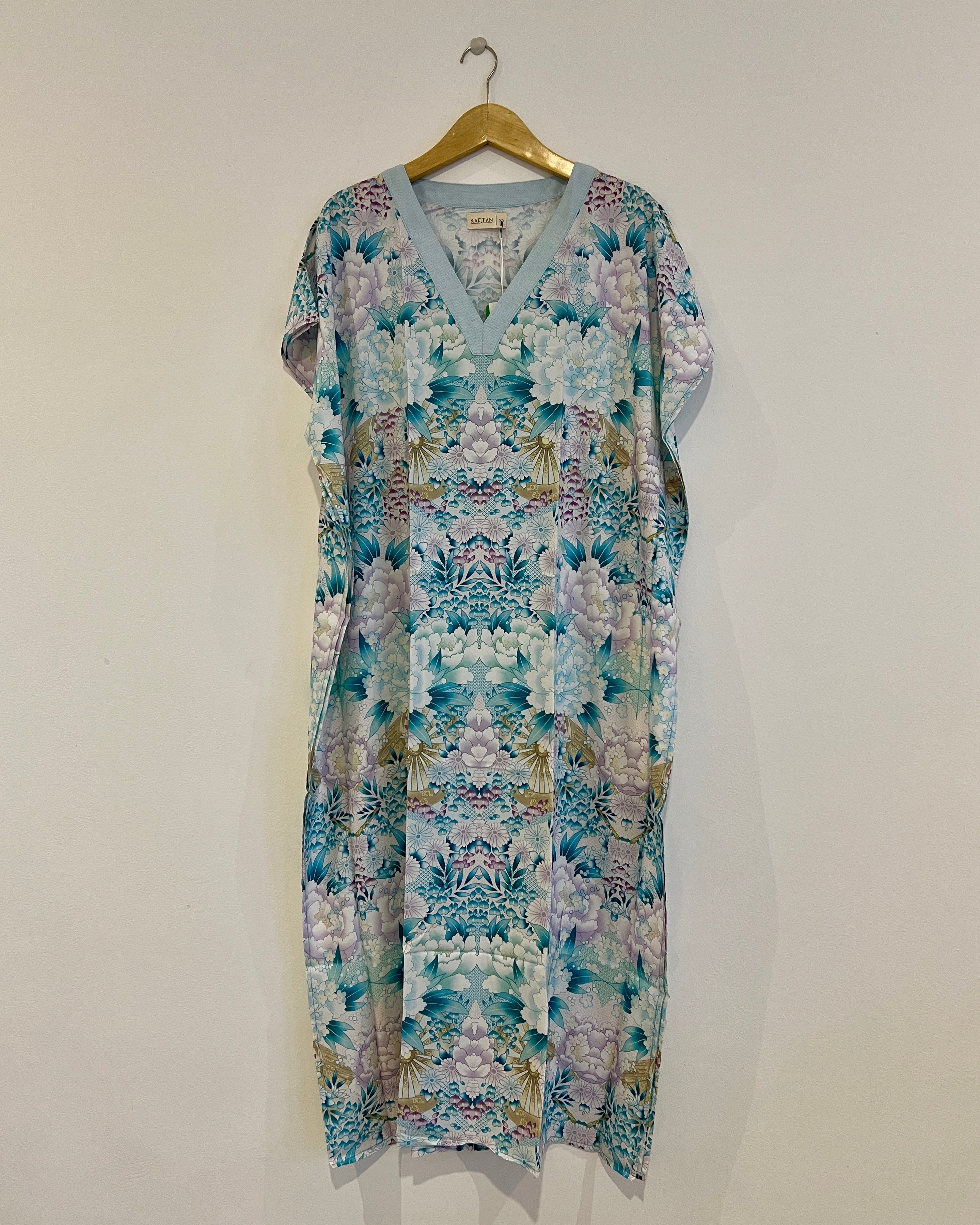 A long kaftan with a floral pattern in shades of green and pink, displayed on a hanger against a white wall.