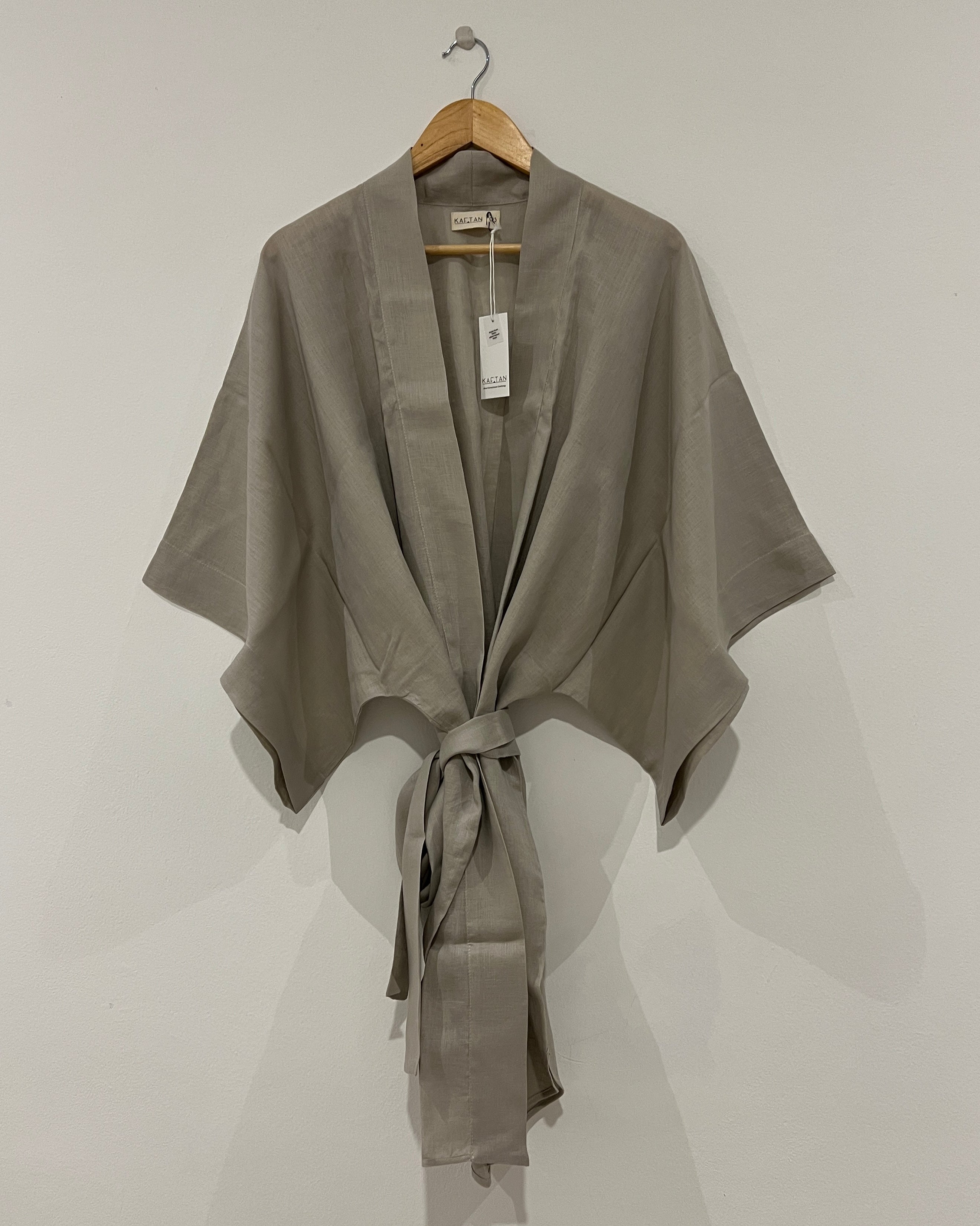 A natural beige kimono robe with extra wide sleeves and a waist tie, displayed on a hanger against a white background.