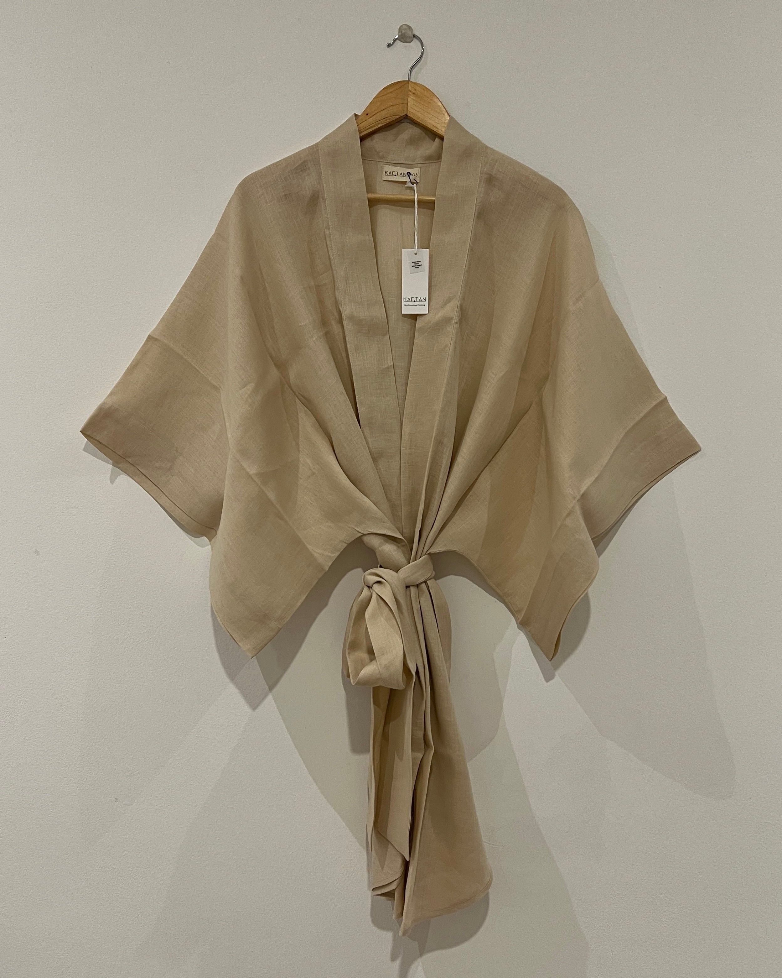 A beige kimono robe with extra wide sleeves and a waist tie, displayed on a hanger against a white background.